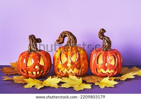 Luminous Ceramic Pumpkin jack lanterns with yellow autumn leaf on purple background. Halloween party decorations