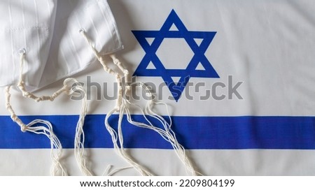 The tallit katan (Hebrew tallis koton, small tallit) with the flag of Israel background. Tallith katan - cape with brushes. Traditions, ritual object. Jewish holiday of Sukkot, shabbat, rosh hashanah Royalty-Free Stock Photo #2209804199