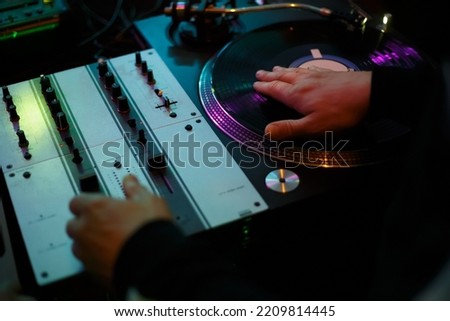 Hip hop dj scratching vinyl record with music on party in night club. Professional disc jockey scratches records on turntables in nightclub. Disk jokey mixing musical tracks on rap concert  Royalty-Free Stock Photo #2209814445