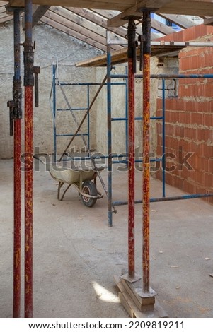 A inside a house under construction, you can see a wheelbarrow, scaffolding and props.