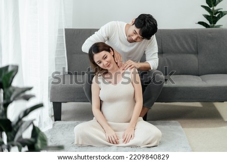 A beautiful pregnant asian woman gets shoulder massaging and loving smile from her husband, a happy asian couple, the concept of taking care of pregnant woman.
