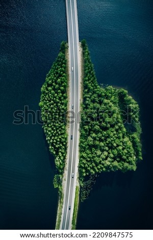 Aerial view of road through blue lakes or sea with green summer woods in Finland.