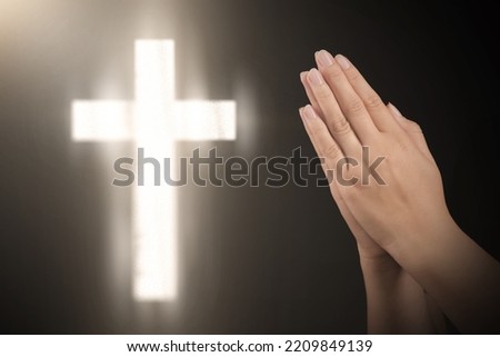 Christian cross and woman holding hands clasped while praying against black background, closeup