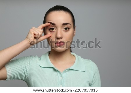 Woman checking her health condition on grey background. Yellow eyes as symptom of problems with liver Royalty-Free Stock Photo #2209859815