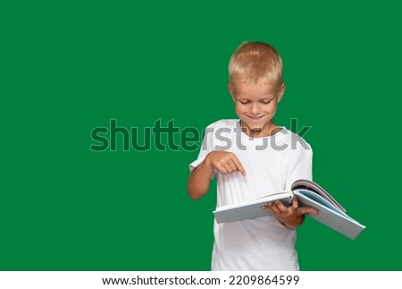 Boy smiles and points to open book with his finger. Green background with space for text. Selective focus. Picture for articles and advertisements about children, reading, education.
