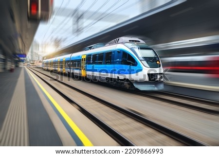 High speed train in motion on the train station at sunset. Blue modern intercity passenger train with motion blur effect. Railway platform. Railroad in Europe. Commercial transportation. Concept Royalty-Free Stock Photo #2209866993