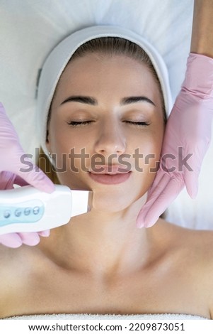Attractive woman receiving ultrasonic facial cleansing cosmetic procedure in beauty salon, top view. Cosmetologist beautician doing ultrasound face treatment to clean skin pores, Cosmetology concept Royalty-Free Stock Photo #2209873051