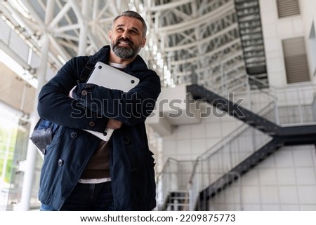 portrait of a successful adult Gray-haired businessman with a laptop in his hands on the background of the airport Waiting room, Concept freelancing and remote work