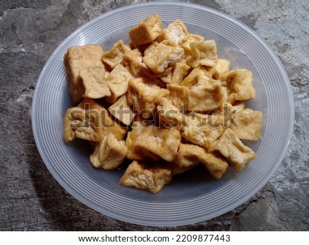 Tahu goreng. Tofu is cut into small squares in a plate on cement floor background. Closeup photo.