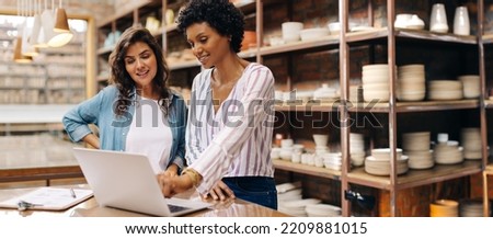 Young female ceramists using a laptop while working together. Two female entrepreneurs managing online orders in their store. Happy young businesswomen running a successful small business together. Royalty-Free Stock Photo #2209881015