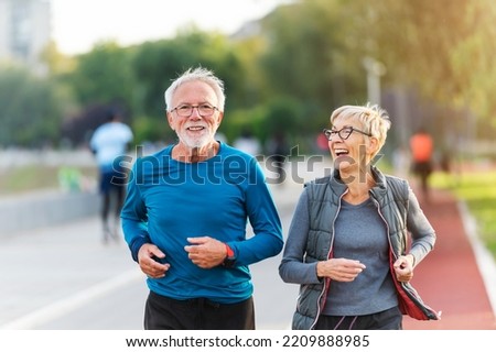 Cheerful active senior couple jogging together outdoors along the river. Healthy activities for elderly people. Royalty-Free Stock Photo #2209888985