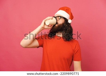 Photo of young bearded man wearing santa claus red hat drinking cup of coffee