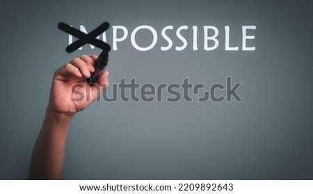 Hand with pen changing the word impossible to possible with cross out im text.