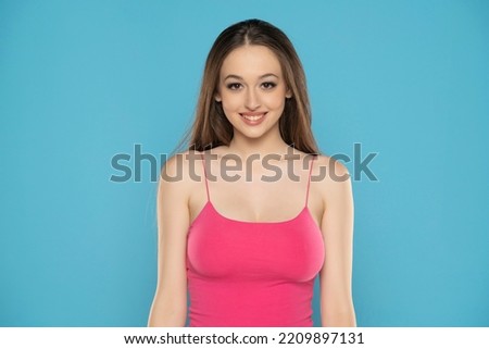 Young woman with pink summer shirt posing in the studio on blue background.