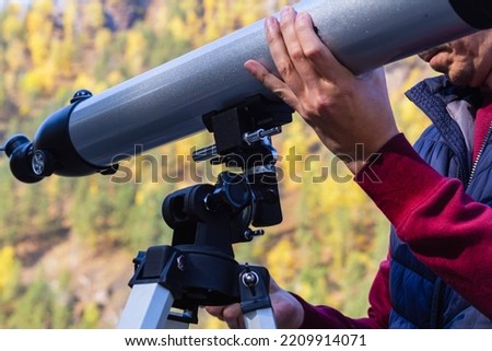Man's hand holds large gray telescope, watch celestial body. Optical telescope, device instrument for land lunar or planetary observation of distant object, magnified by lenses. Royalty-Free Stock Photo #2209914071