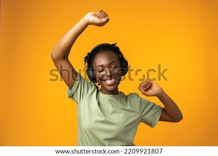 Happy young woman listening to music in headphones against yellow background Royalty-Free Stock Photo #2209921807
