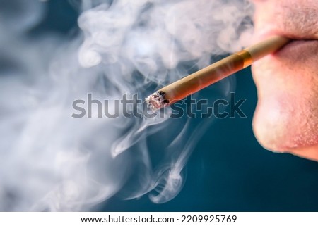 A man holds a cigarette in his mouth. He blew out puffs of smoke.
