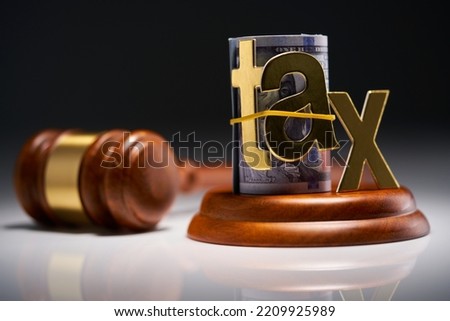 Judge's gavel with dollars in roll with single word tax  against gray background Royalty-Free Stock Photo #2209925989