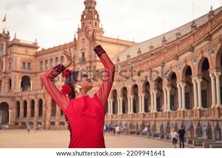 Beautiful teenage woman dancing flamenco in a square in Seville, Spain. She wears a red dress with ruffles and dances flamenco with a lot of art. Flamenco cultural heritage of humanity. Royalty-Free Stock Photo #2209941641