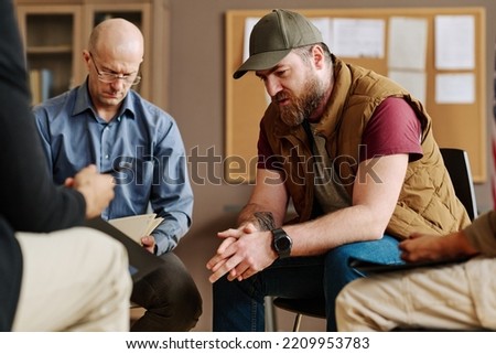 Young upset man describing traumatic event or experience from his life while sitting among counselor and other attendants of session Royalty-Free Stock Photo #2209953783