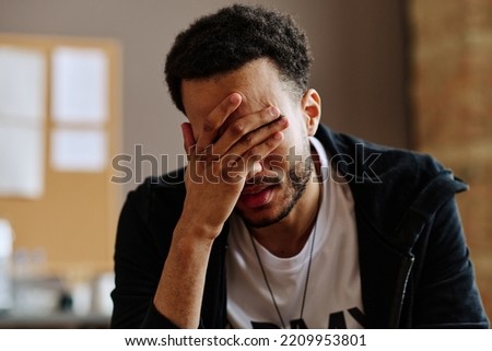 Young depressed man touching face while suffering from post traumatic syndrome and describing his problems at psychological session Royalty-Free Stock Photo #2209953801