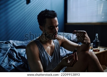 Young man with post traumatic syndrome looking at metallic medallion on chain while thinking of event or person it reminds him of Royalty-Free Stock Photo #2209953893