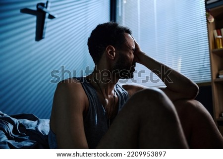 Young stressed man touching head while sitting by bed after sleepless night and feeling helpless about consequences of PTSD Royalty-Free Stock Photo #2209953897