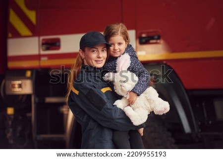 Against big truck. With bunny toy. Firefighter woman in uniform is with a little girl.
