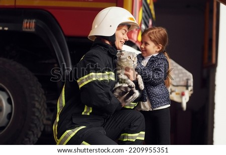 Giving beautiful scottish fold cat. Firefighter woman in uniform is with a little girl.