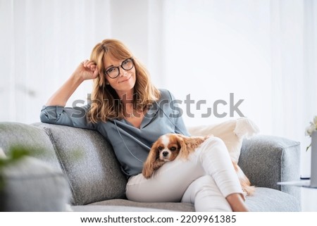 Shot of happy middle aged woman relaxing on the sofa at home with her cavalier puppy. Royalty-Free Stock Photo #2209961385