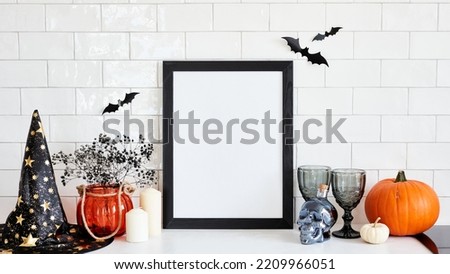 Black picture frame mockup with Halloween decorations on table on brick wall background. Scandinavian home interior design. Halloween holiday celebration concept.