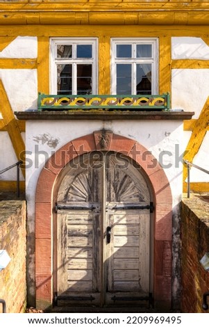 A closed gate with double door, round arch and windows above it in the facade of an old half-timbered house
