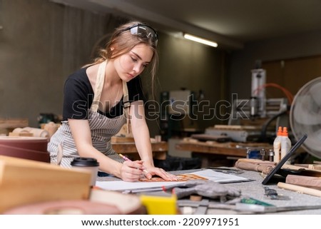 Portrait of a female carpenter drawing on paper for designing and building furniture in a furniture factory. with modern tools Royalty-Free Stock Photo #2209971951