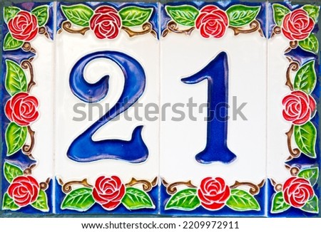 Close up of a house number 21 on enameled colorful tiles with symbolized red rose petals