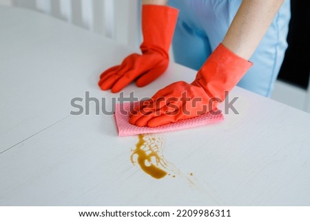 women hands cleaning tea stain or spilled coffee on a white table with a yellow dishcloth closeup Royalty-Free Stock Photo #2209986311