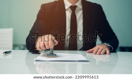 Close-up of a person's hand stamping with approved stamp on certificate document at desk Royalty-Free Stock Photo #2209995613
