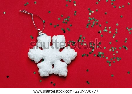 White big snowflake and small green twinkling decorative shiny stars shine on red surface. View from above. Christmas and new year celebration concept. Copy space for text.