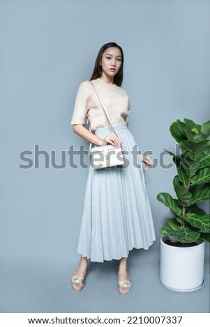 fashion asian girl wears knit long sleeve tops and blue long skirt with white leather handbag and silver sandals Royalty-Free Stock Photo #2210007337