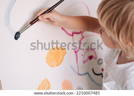 Child is painting with paintbrush. Child drawing on the easel. The hand and paint brush. Closeup, selective focus.