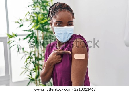 Beautiful black woman getting vaccine showing arm with band aid smiling happy pointing with hand and finger 
