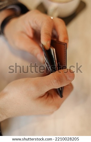 Brown leather wallet with a compartment for credit cards in his hands, manufacture and sale of leather goods, a man holds a purse with money in his hands, leather business