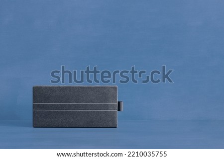 A stylish textured rectangular cardboard box with two thin white lines down the middle on a blue-painted studio background with copy space. Gift and packaging concept.