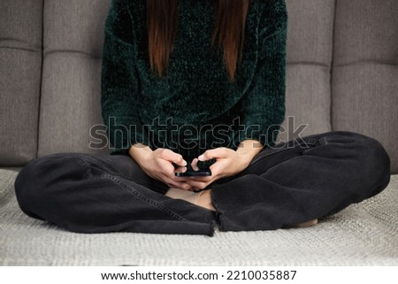 Girl typing sms message on mobile phone. Young woman sitting on couch and communicating on social media app in smartphone. Stock photo of female person using modern cellphone 