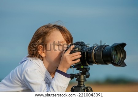 Blonde little girl taking pictures with a big camera standing on a tripod.