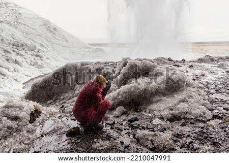 Girl taking pictures behind the waterfall with ice