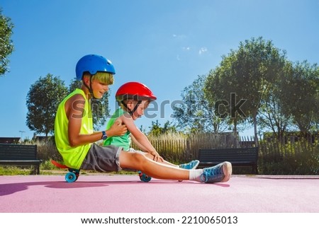Side view of two brothers sit on the skate at skatepark playing and riding on the ramp