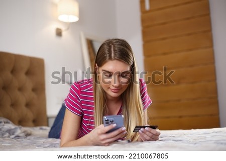 Young woman paying online with credit card. Female buying in mobile app with smartphone and bank card. Stock photo of blond girl making money transfer online with mobile application in cellphone