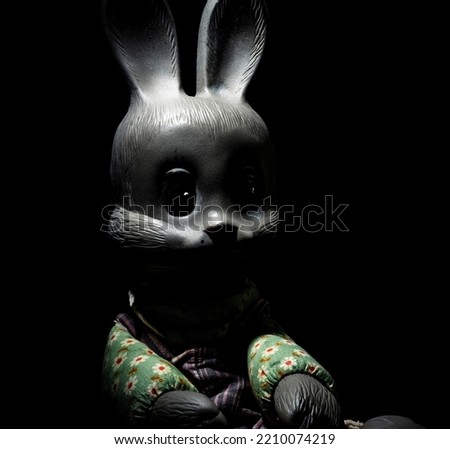 Spooky rabbit sits in the dark. Creepy toy bunny face. Rabbit doll in a very dark room