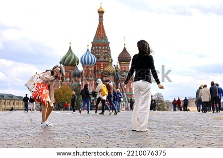 Two girls tourists taking pictures on Red square in Moscow, view to St. Basil's Cathedral in autumn