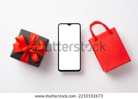 Cyber monday concept. Top view photo of smartphone red paper bag and giftbox with ribbon bow on isolated white background with copyspace